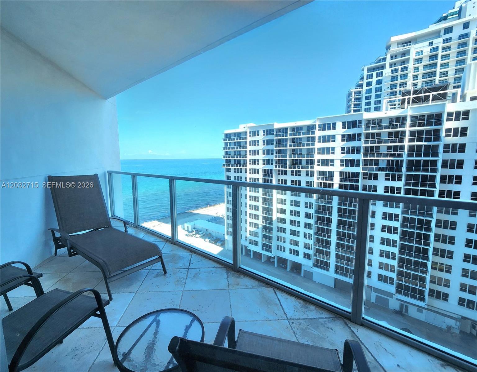 A balcony with patio furniture overlooks the ocean and a neighboring high-rise building — 3101 S Ocean Dr # 1106, Hollywood FL 33019, HOLLYWOOD, FL