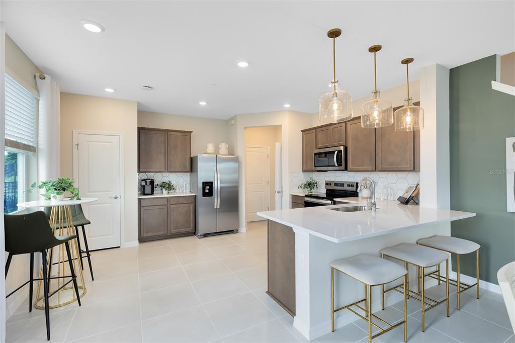 A modern kitchen features gray cabinets, white countertops, a central island, and three pendant lights — 3242 PONDSIDE WAY, SANFORD, FL