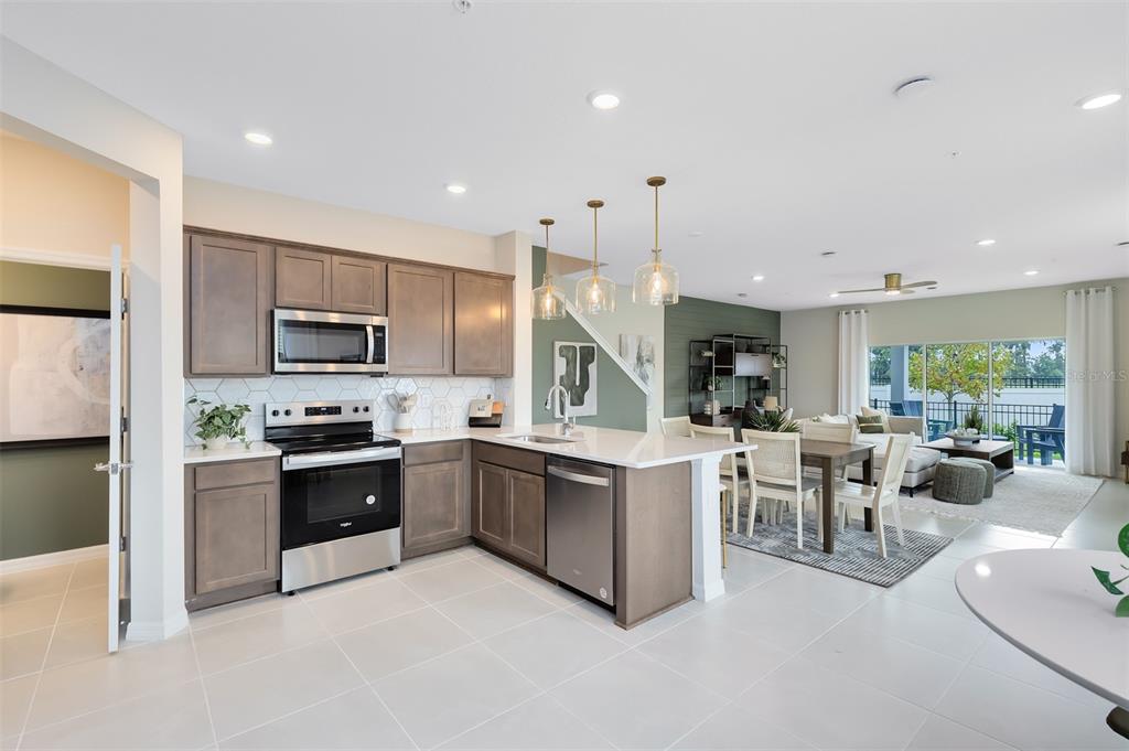 A modern kitchen with wood cabinets and stainless steel appliances opens to a dining area — 3242 PONDSIDE WAY, SANFORD, FL