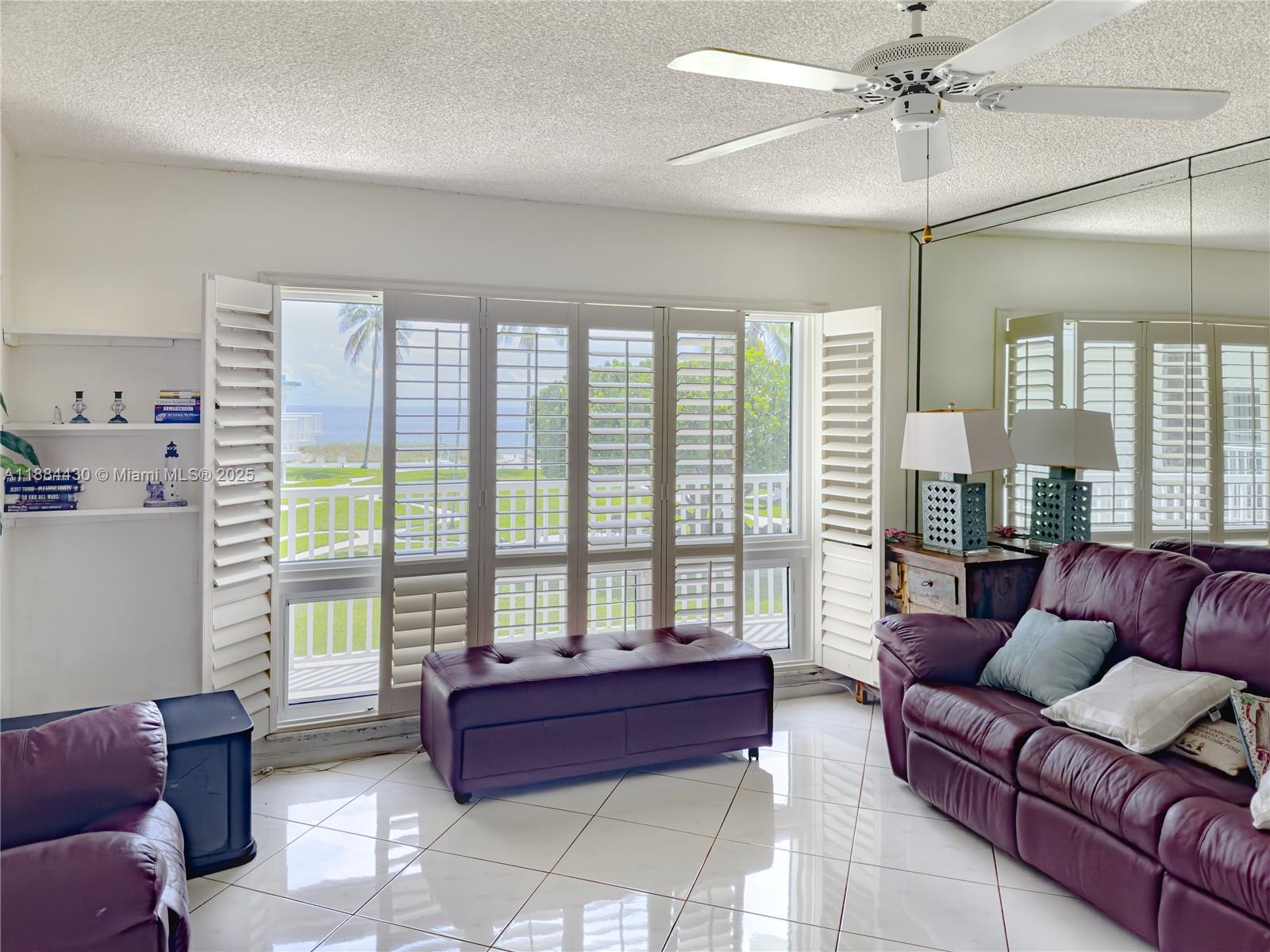 A living room with white tile floors, a purple leather sofa, and plantation shutters overlooking water — 1470 S Ocean Blvd # 702, Pompano Beach FL 33062, POMPANO BEACH, FL