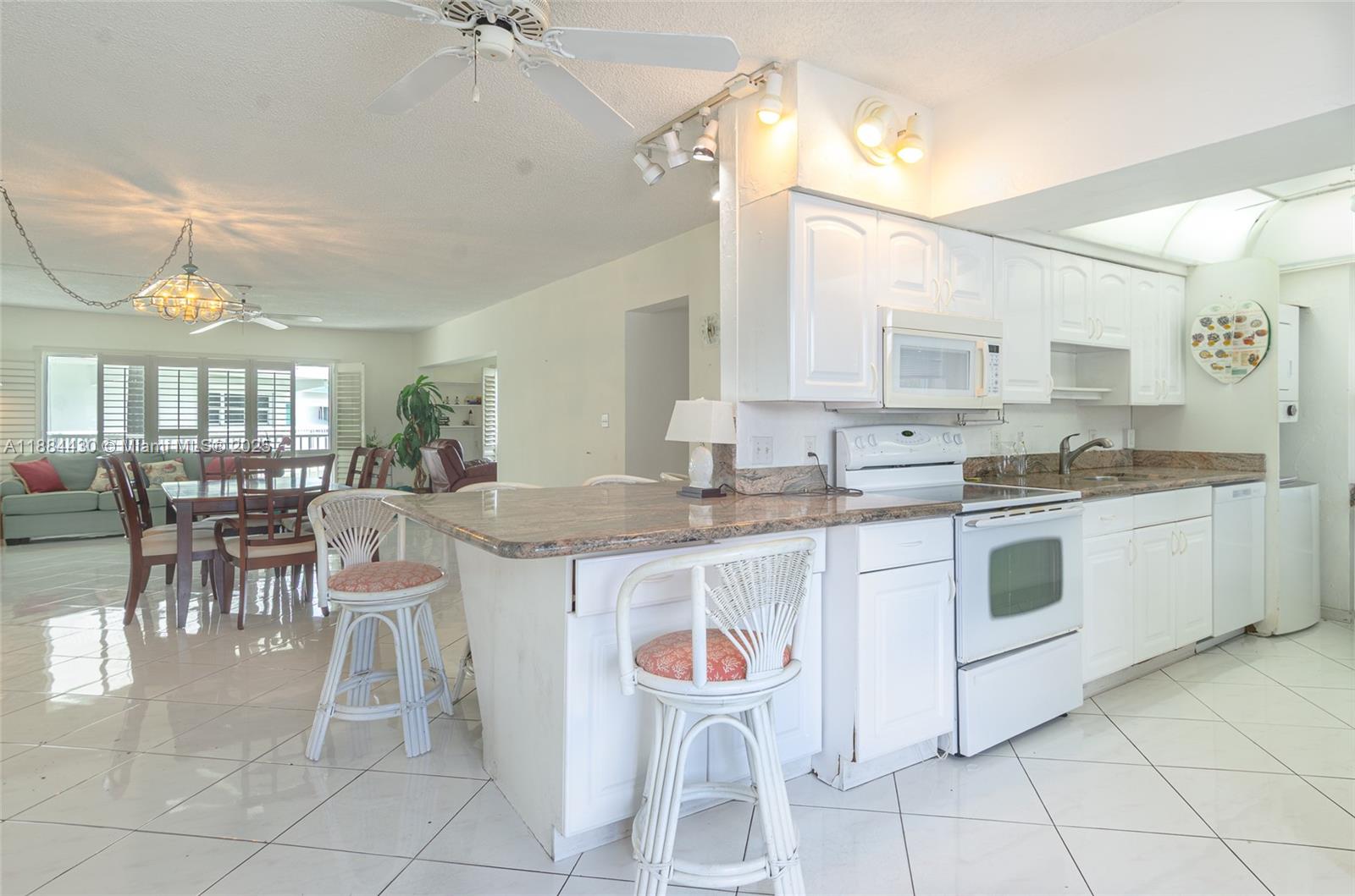A kitchen with white cabinets and granite countertops overlooks a dining area and living room — 1470 S Ocean Blvd # 702, Pompano Beach FL 33062, POMPANO BEACH, FL