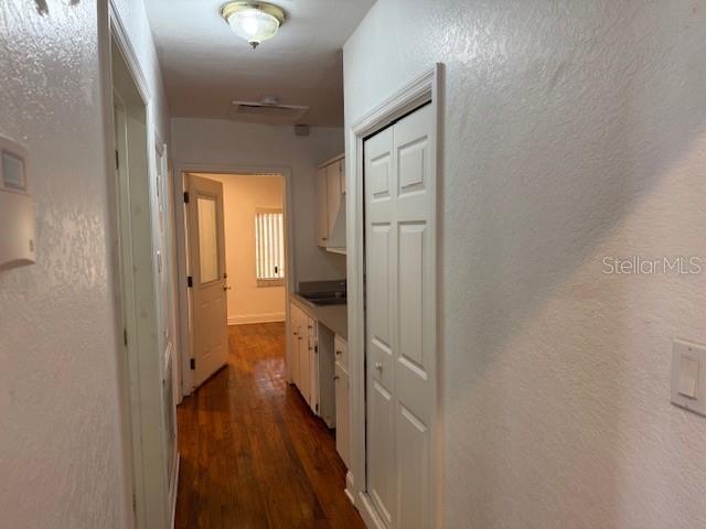 A hallway with hardwood floors leads to a kitchen with white cabinets and a door — 207 N CHURCH AVENUE UNIT 207, MULBERRY, FL