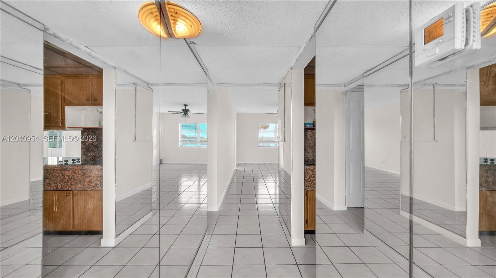 A tiled hallway features mirrored walls reflecting a kitchen and an adjacent living area — 251 NE 187th St # 830, Miami FL 33179, MIAMI, FL
