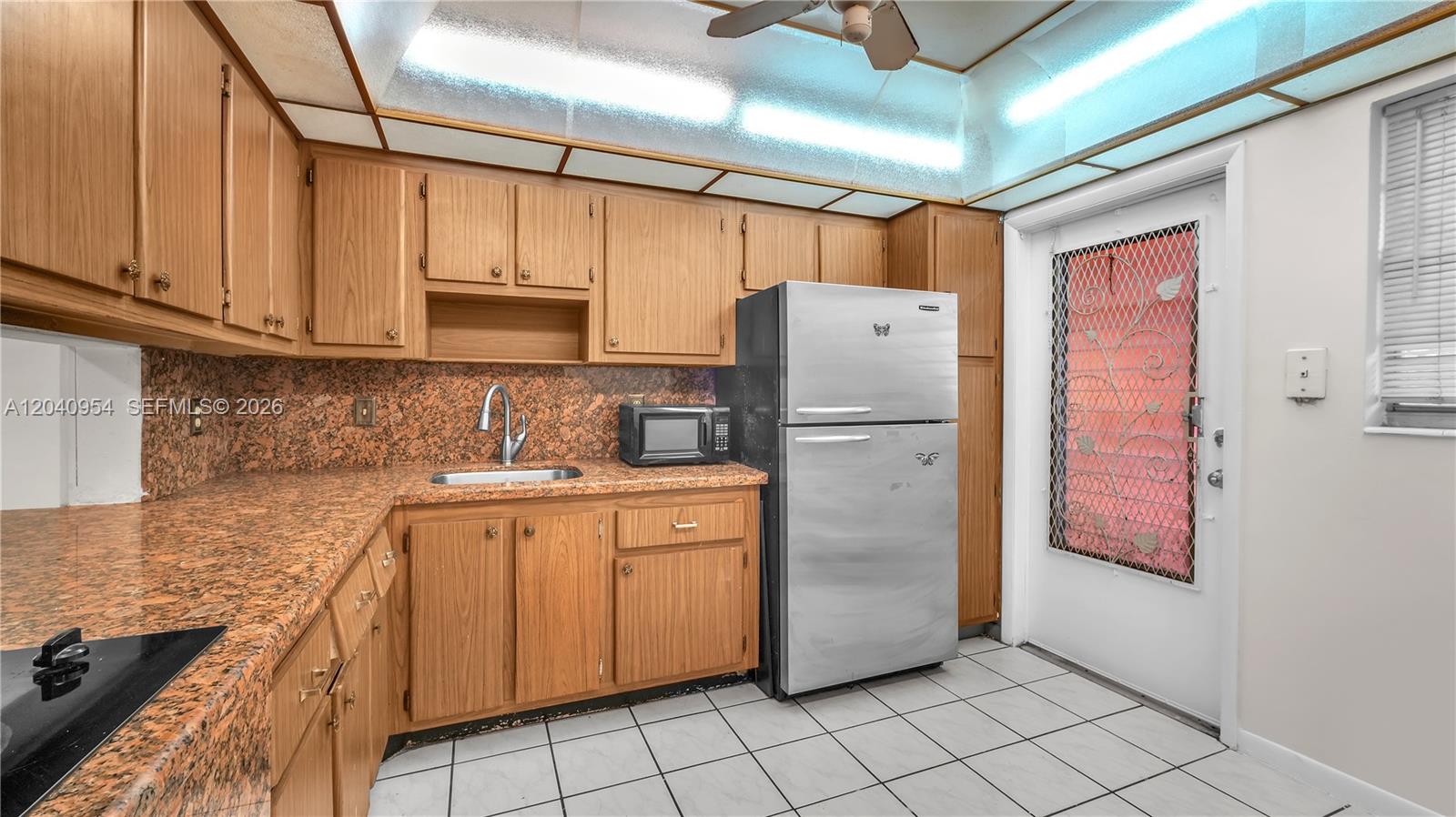 A kitchen features wood cabinets, granite countertops, a stainless steel refrigerator, and a glass door — 251 NE 187th St # 830, Miami FL 33179, MIAMI, FL