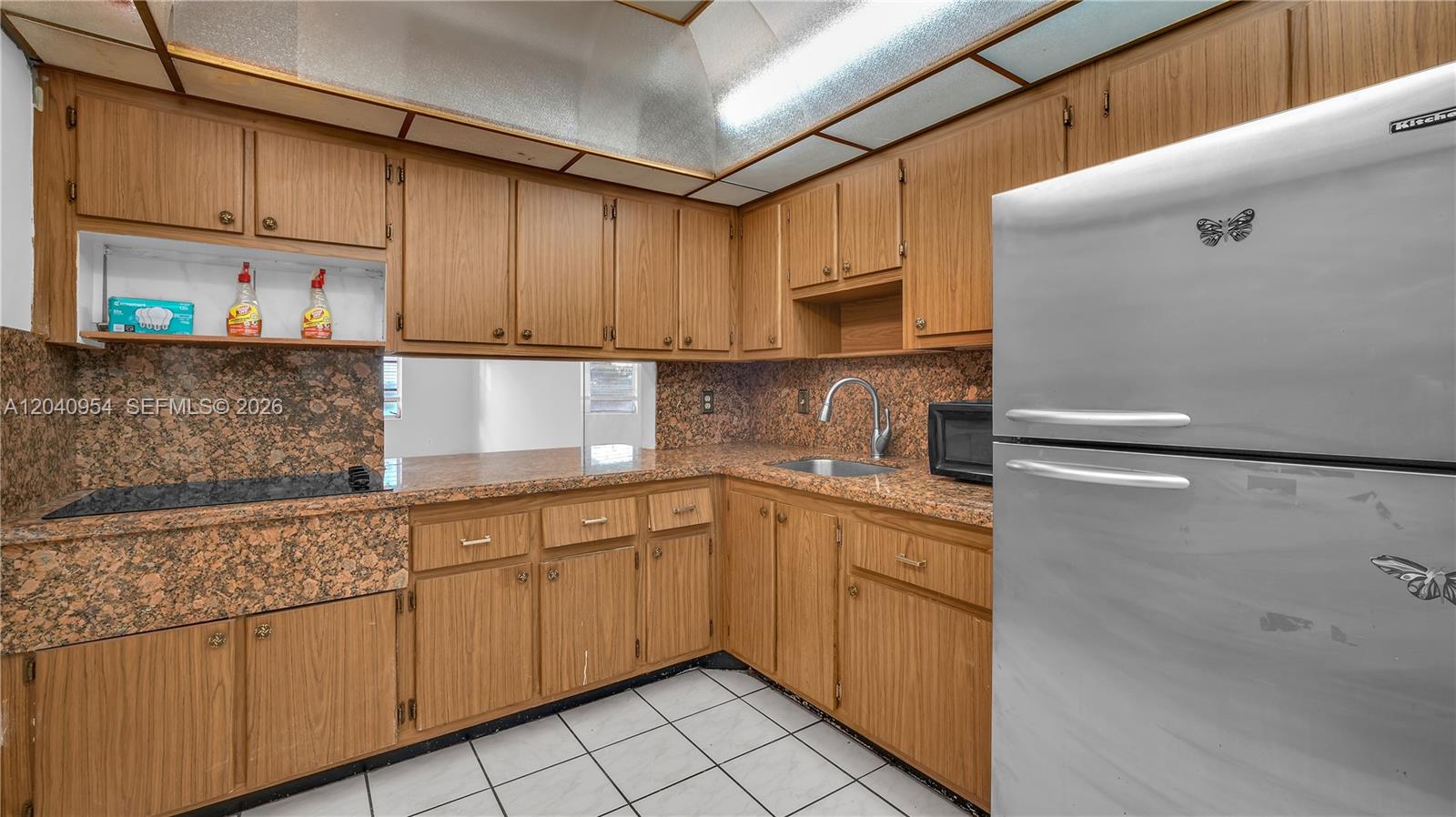 A kitchen features wood cabinets, granite countertops, a stainless steel sink, and white tile flooring — 251 NE 187th St # 830, Miami FL 33179, MIAMI, FL
