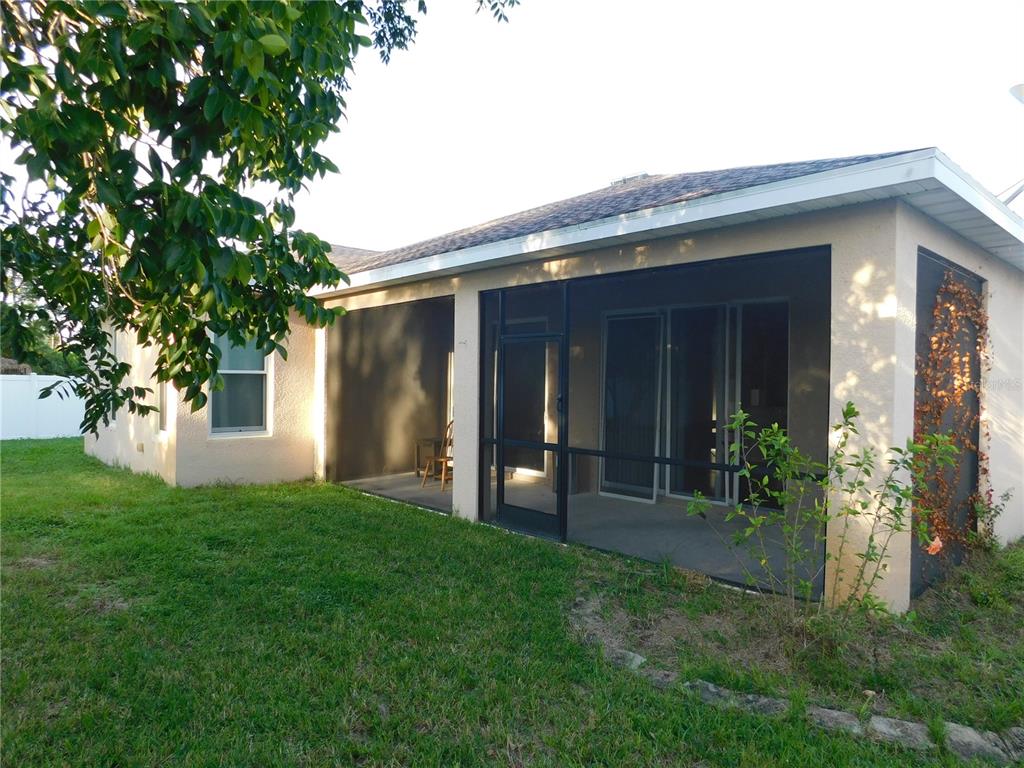 A beige house features a screened-in back porch with sliding glass doors and a lawn — 2507 HOBBLEBRUSH DRIVE, NORTH PORT, FL