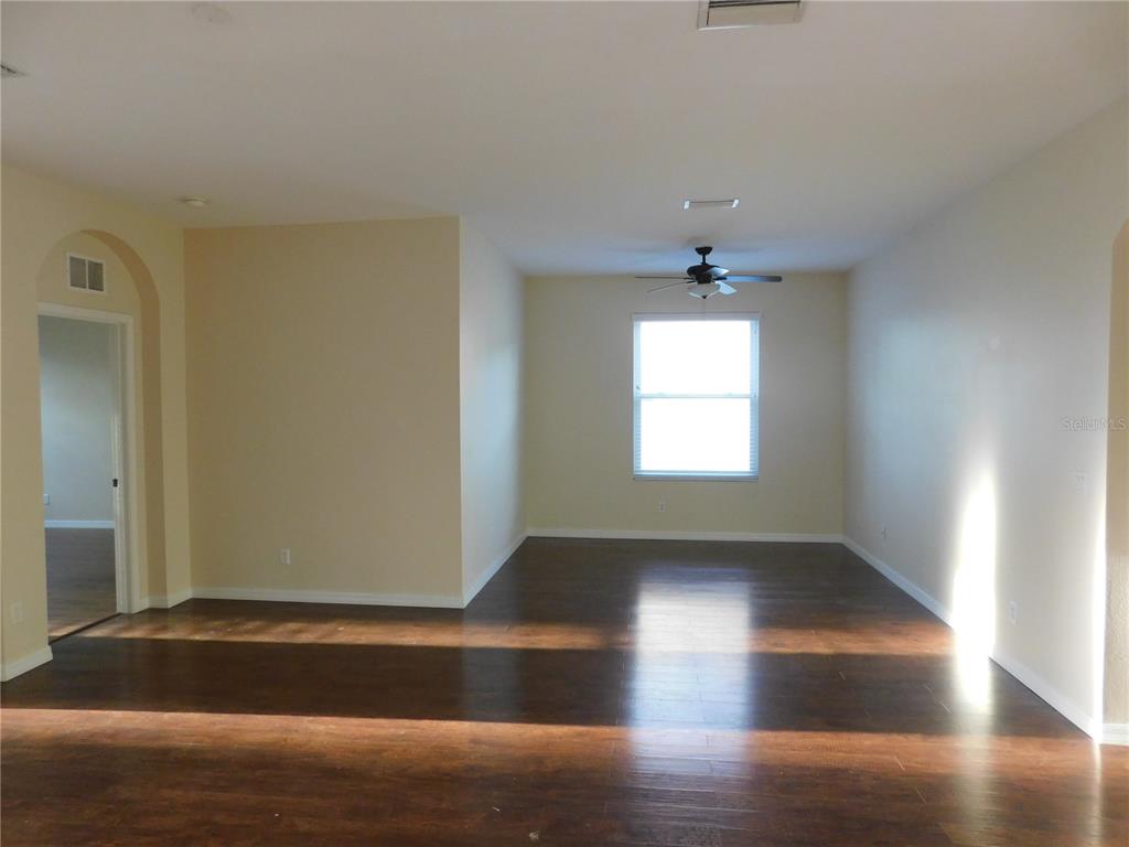 An empty room with dark wood flooring, beige walls, a ceiling fan, and a window — 2507 HOBBLEBRUSH DRIVE, NORTH PORT, FL