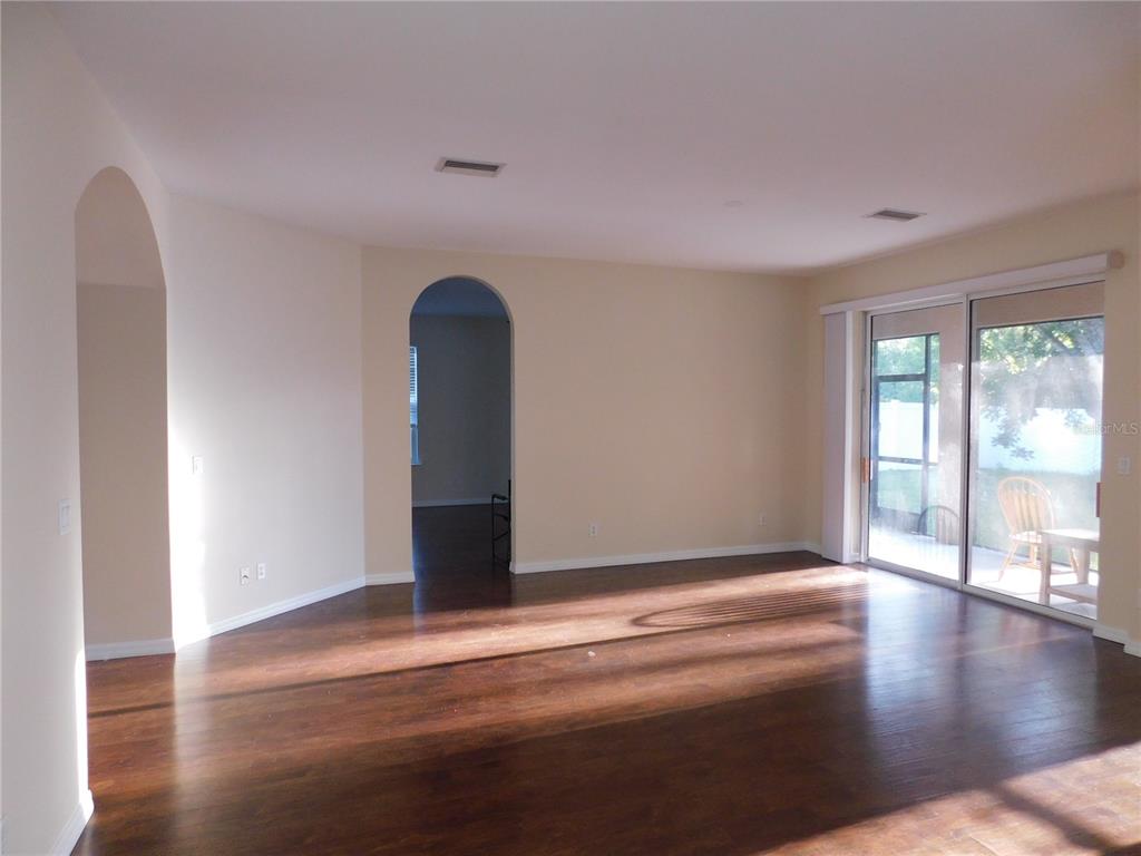 An empty living room features dark wood flooring, arched doorways, and sliding glass patio doors — 2507 HOBBLEBRUSH DRIVE, NORTH PORT, FL
