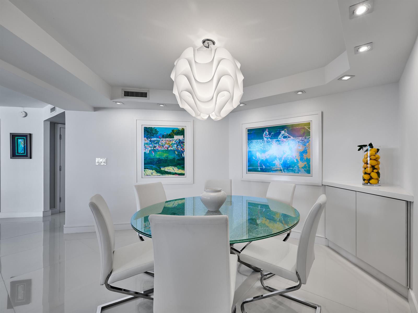 A modern dining room features a glass-topped table, white chairs, and a sculptural pendant light — 550 S Ocean Boulevard # 1405, Boca Raton FL 33432, BOCA RATON, FL