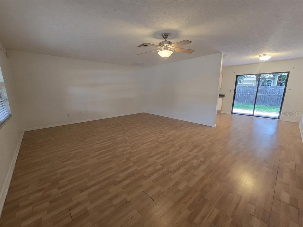 An empty living room with light wood-look flooring, a ceiling fan, and sliding glass doors — 202 JACOB RYAN COURT, BRANDON, FL