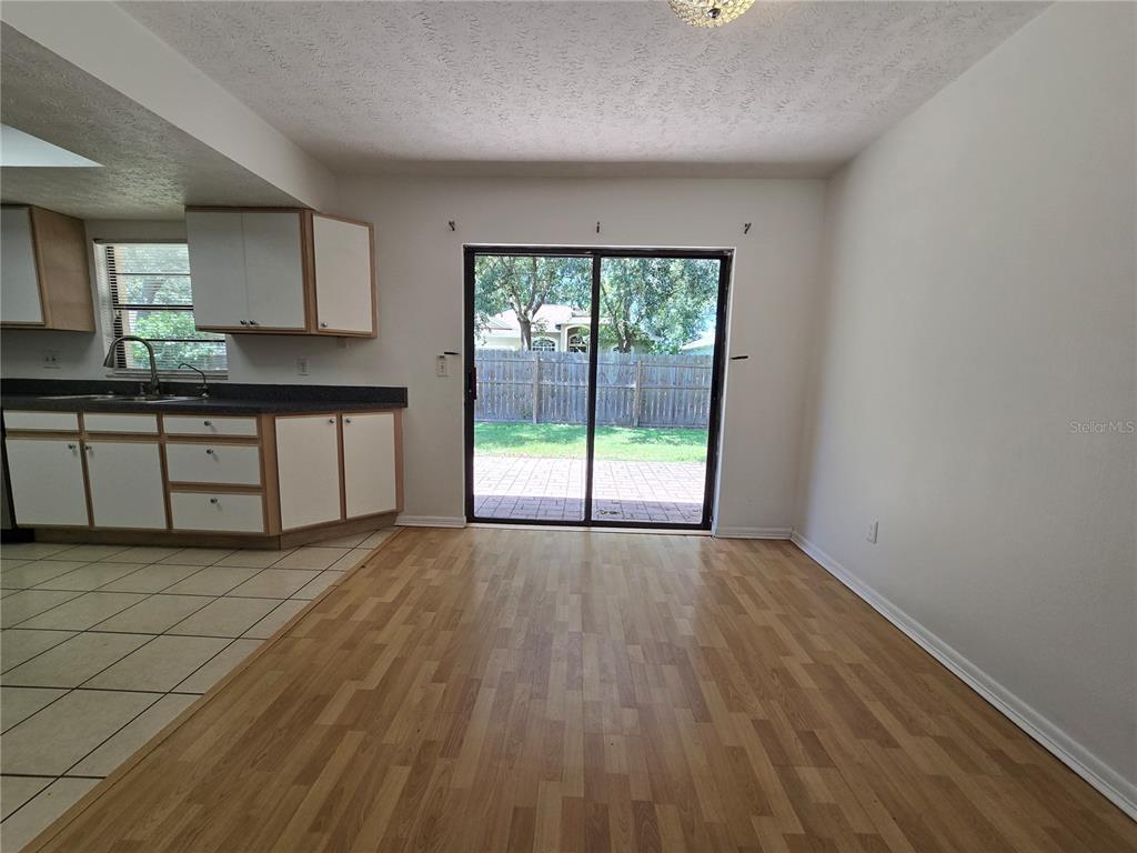 A kitchen with white cabinets and tile flooring transitions into a dining area with wood flooring — 202 JACOB RYAN COURT, BRANDON, FL