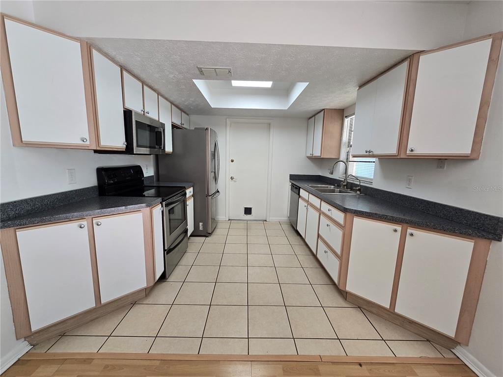 A galley kitchen features white cabinets with wood trim, dark countertops, and stainless steel appliances — 202 JACOB RYAN COURT, BRANDON, FL