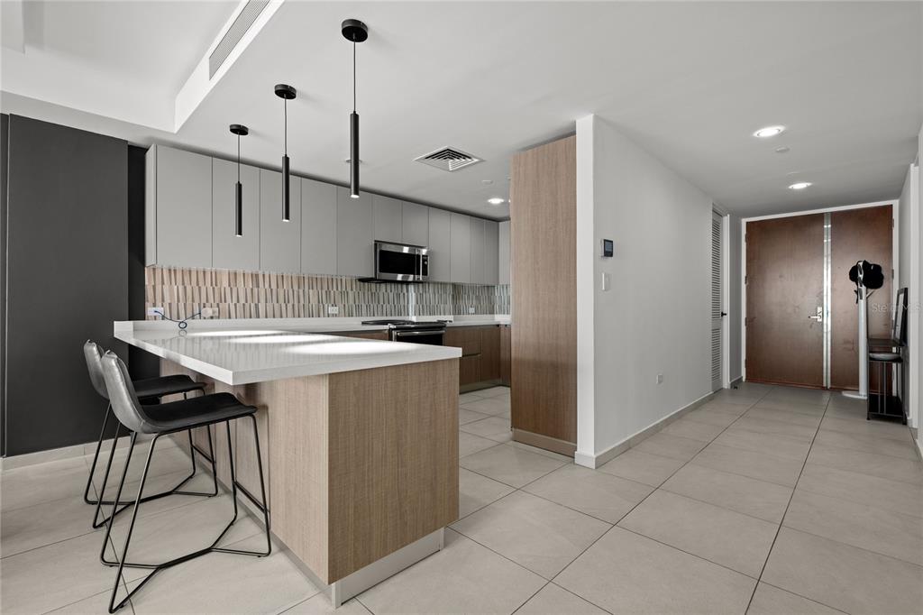 A modern kitchen features light wood cabinetry, gray upper cabinets, and a white breakfast bar — 25 Ave Muñoz Rivera BAHIA PLAZA APT UNIT 616, SAN JUAN, PR