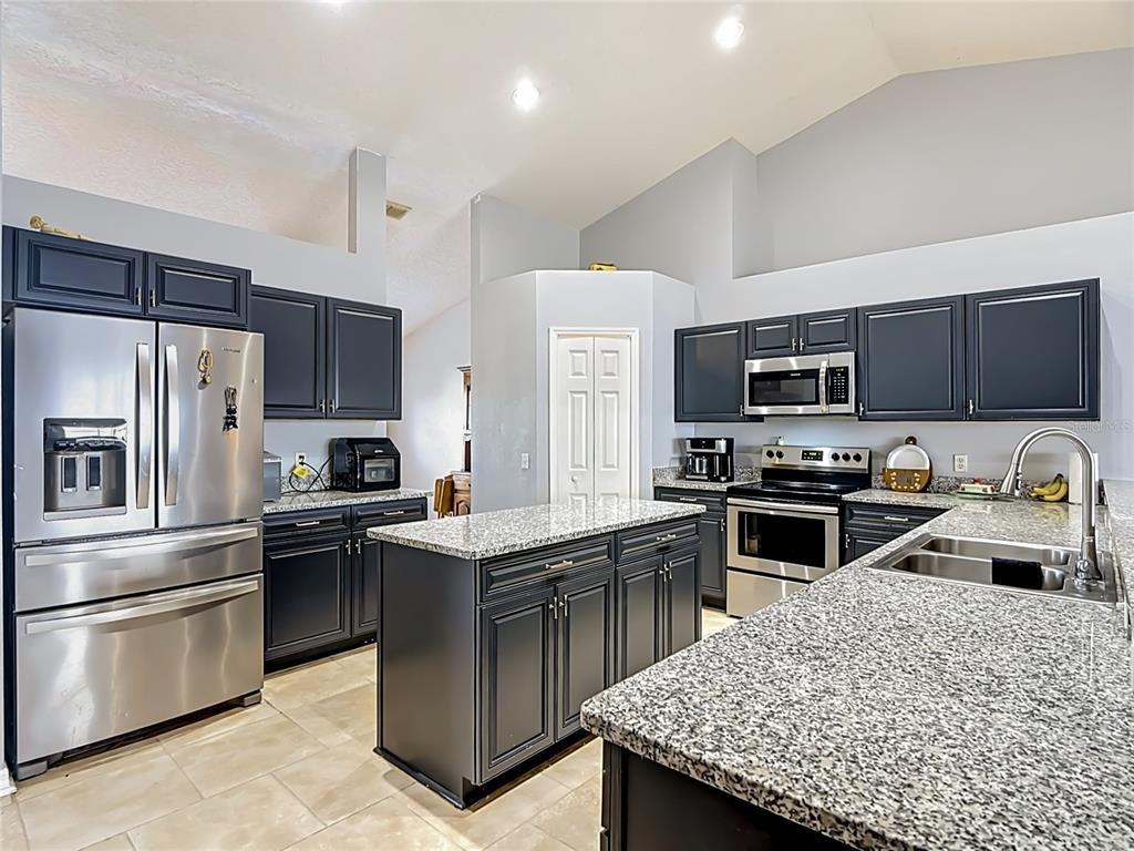 A kitchen features dark cabinets, granite countertops, stainless steel appliances, and a central island — 20 ANDORA COURT, KISSIMMEE, FL