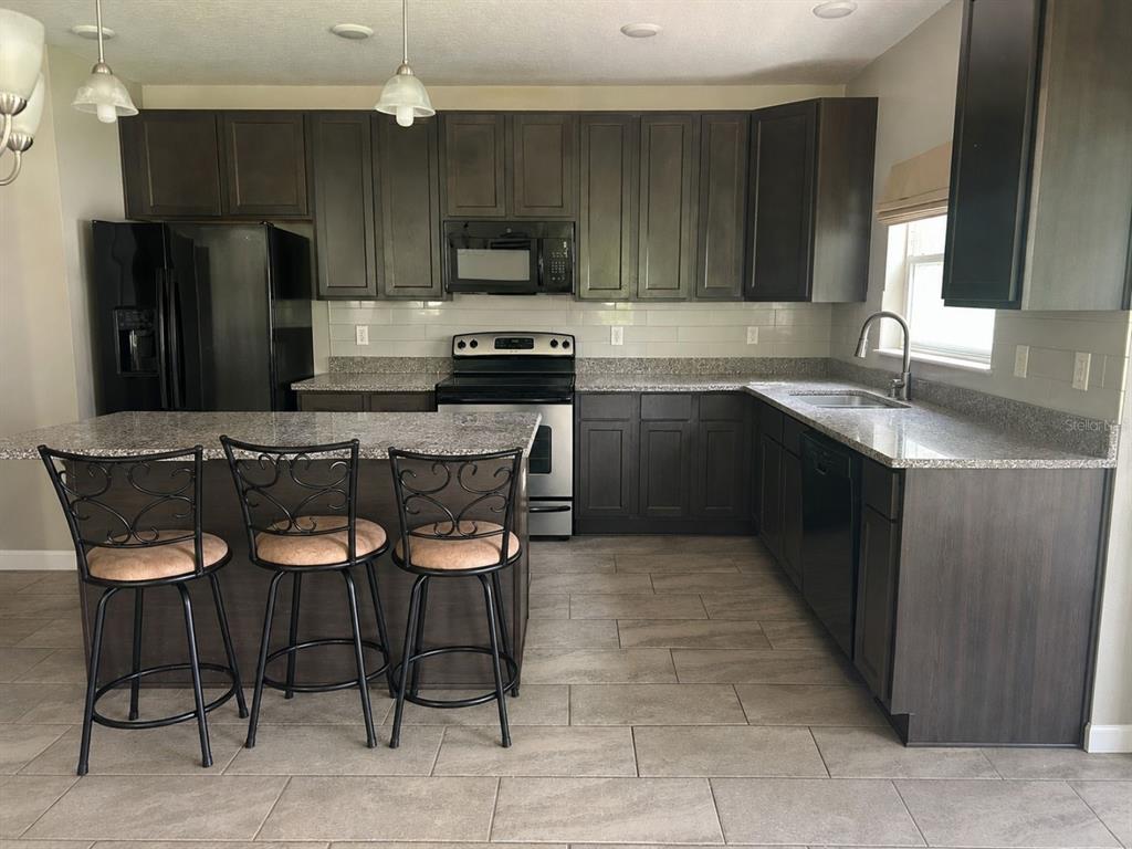 A kitchen features dark wood cabinets, granite countertops, a kitchen island, and stainless steel appliances — 100 ALBANY DRIVE, POINCIANA, FL