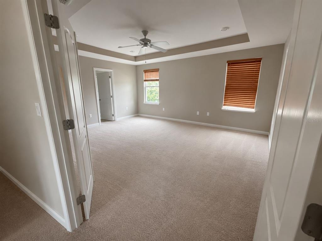 A spacious bedroom with beige carpet, a tray ceiling, and two windows with wood blinds — 100 ALBANY DRIVE, POINCIANA, FL