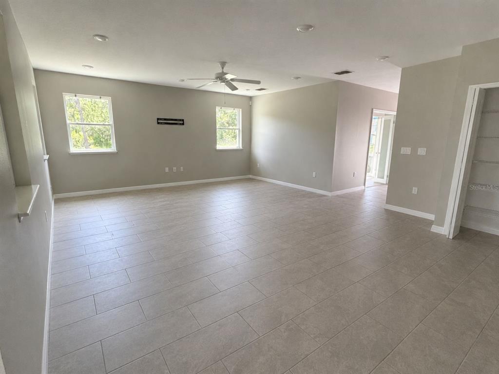 A spacious living room features light gray walls, tile flooring, a ceiling fan, and two windows — 100 ALBANY DRIVE, POINCIANA, FL