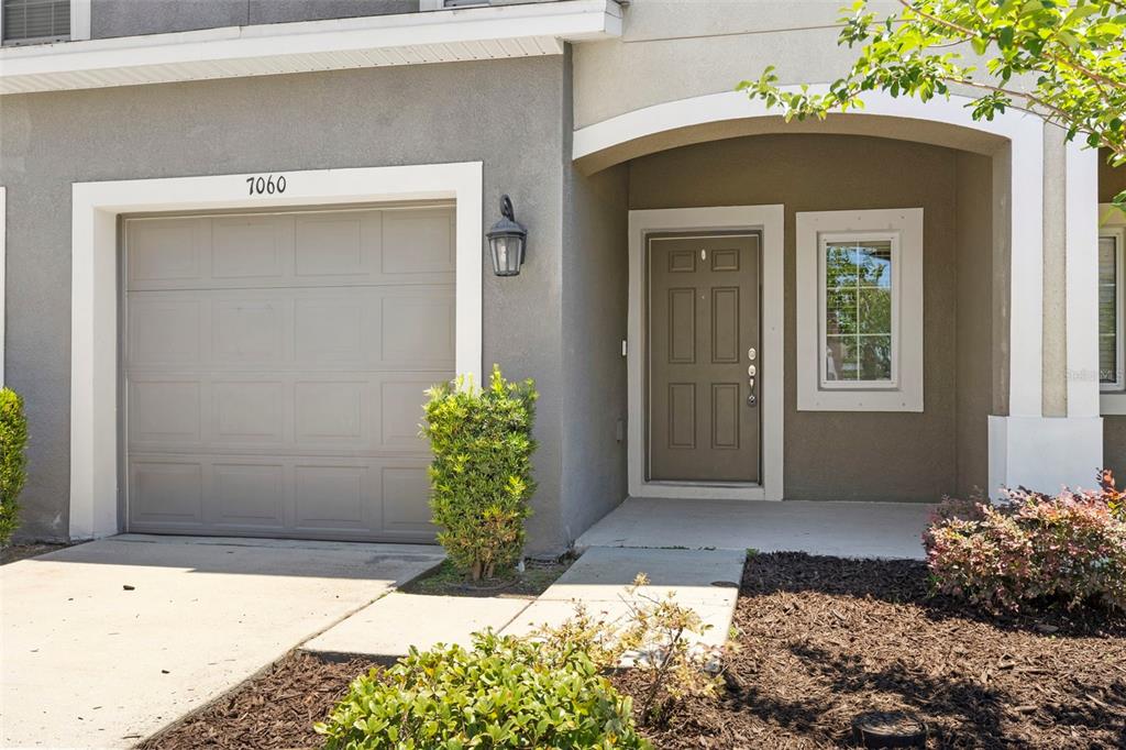 The exterior of a house features a gray garage door, a front door, and landscaping — 7060 WOODCHASE GLEN DRIVE, RIVERVIEW, FL