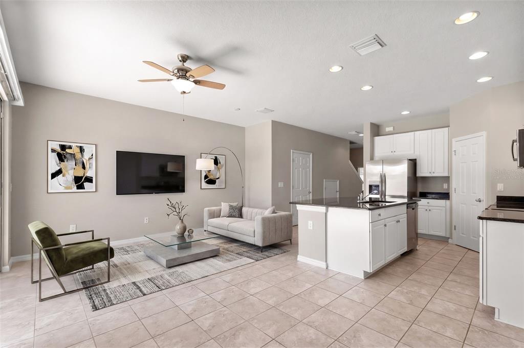 An open-concept living room and kitchen featuring tile floors, a ceiling fan, and white cabinetry — 7060 WOODCHASE GLEN DRIVE, RIVERVIEW, FL