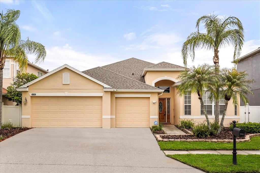 A single-story house with a beige stucco exterior, a three-car garage, and palm trees — 14749 BRUNSWOOD WAY, ORLANDO, FL