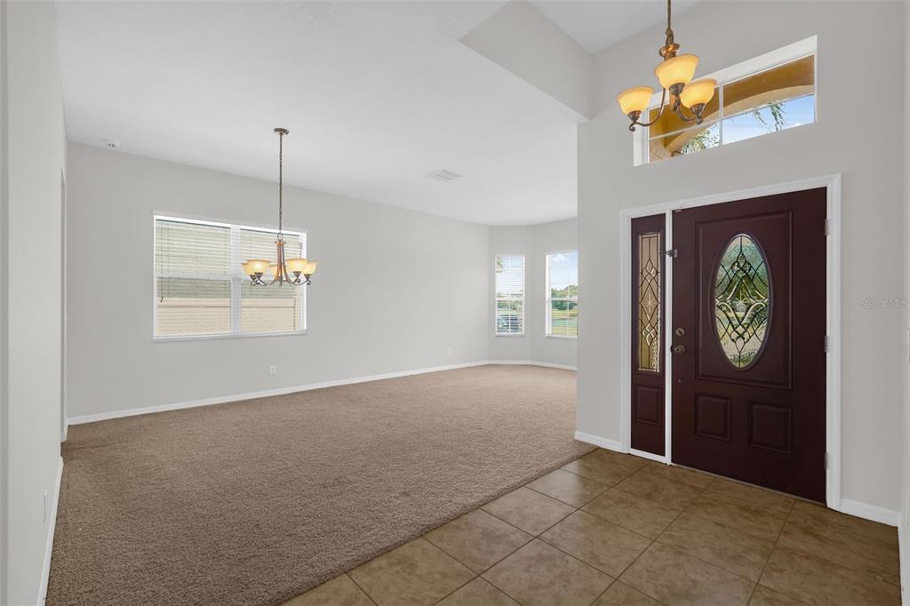 An entryway with tiled floors leads into a carpeted living area with a dining chandelier — 14749 BRUNSWOOD WAY, ORLANDO, FL