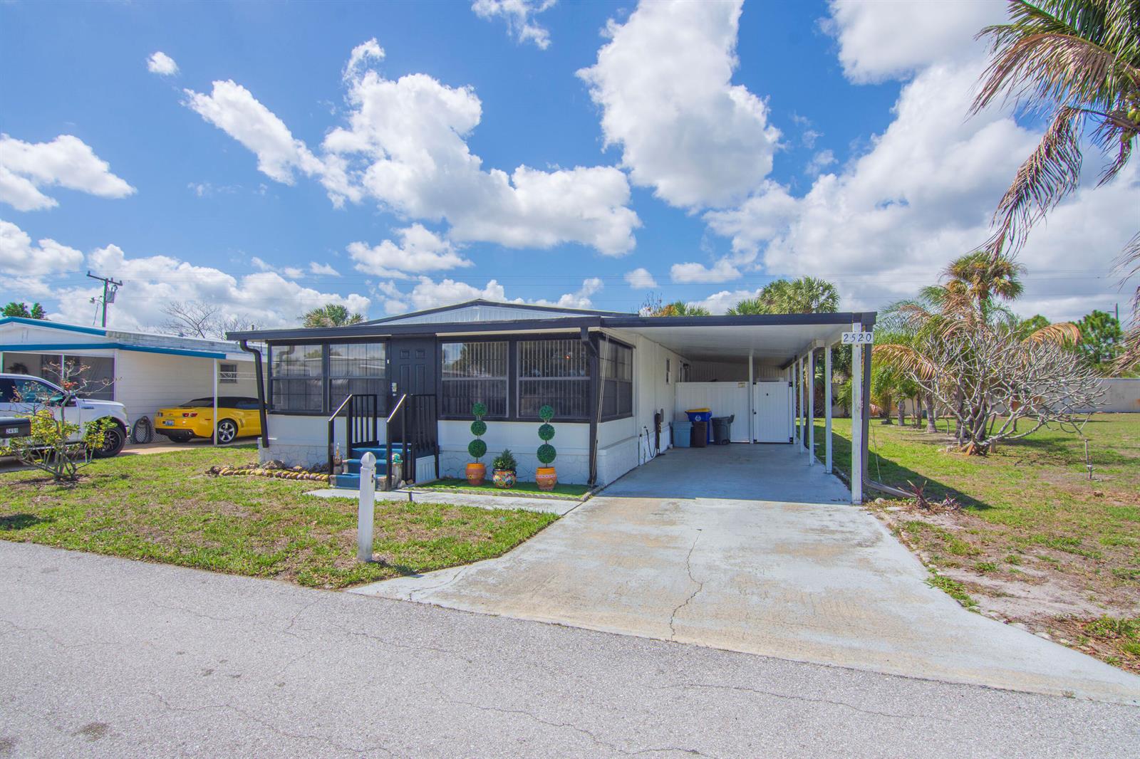 A single-story manufactured home features a carport, a concrete driveway, and a small front porch — 2520 SE Penny Lane, Stuart FL 34994, STUART, FL