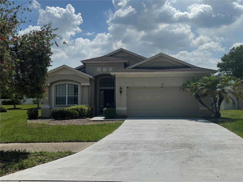 A single-story house with a beige stucco exterior, a two-car garage, and a front lawn — 317 DOWN PINE DRIVE, SEFFNER, FL