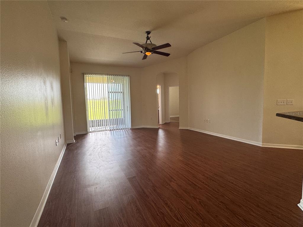 An empty living room features wood-look flooring, a ceiling fan, and sliding glass doors — 317 DOWN PINE DRIVE, SEFFNER, FL