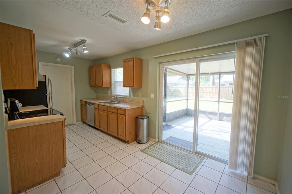 A kitchen with wood cabinets, tile flooring, and a sliding glass door to a patio — 5117 ELLENDALE AVENUE, TAMPA, FL