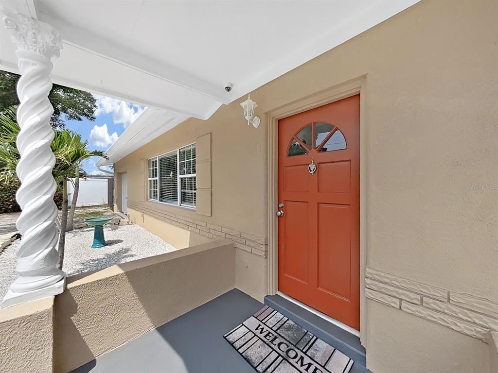 A covered porch features a white spiral column, a terracotta-colored front door, and a welcome mat — 5931 49TH AVENUE N, ST PETERSBURG, FL