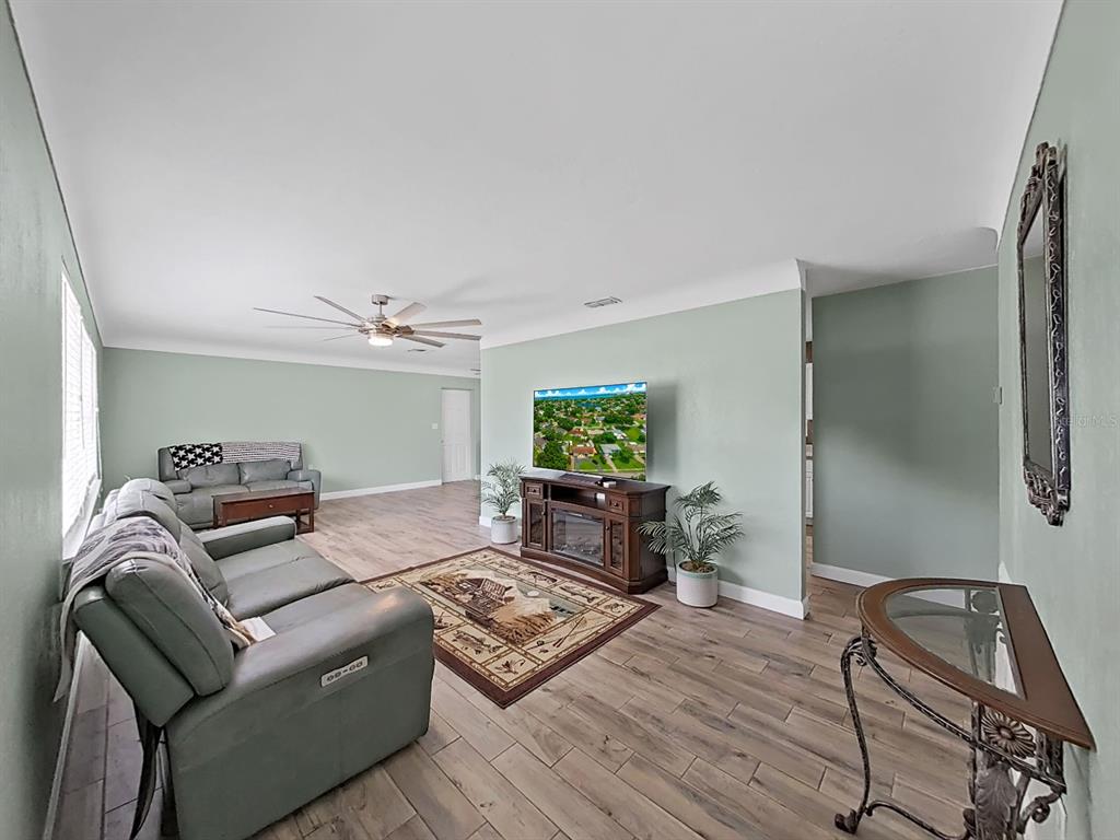 A living room features light green walls, wood-look flooring, a television, and two gray sofas — 5931 49TH AVENUE N, ST PETERSBURG, FL