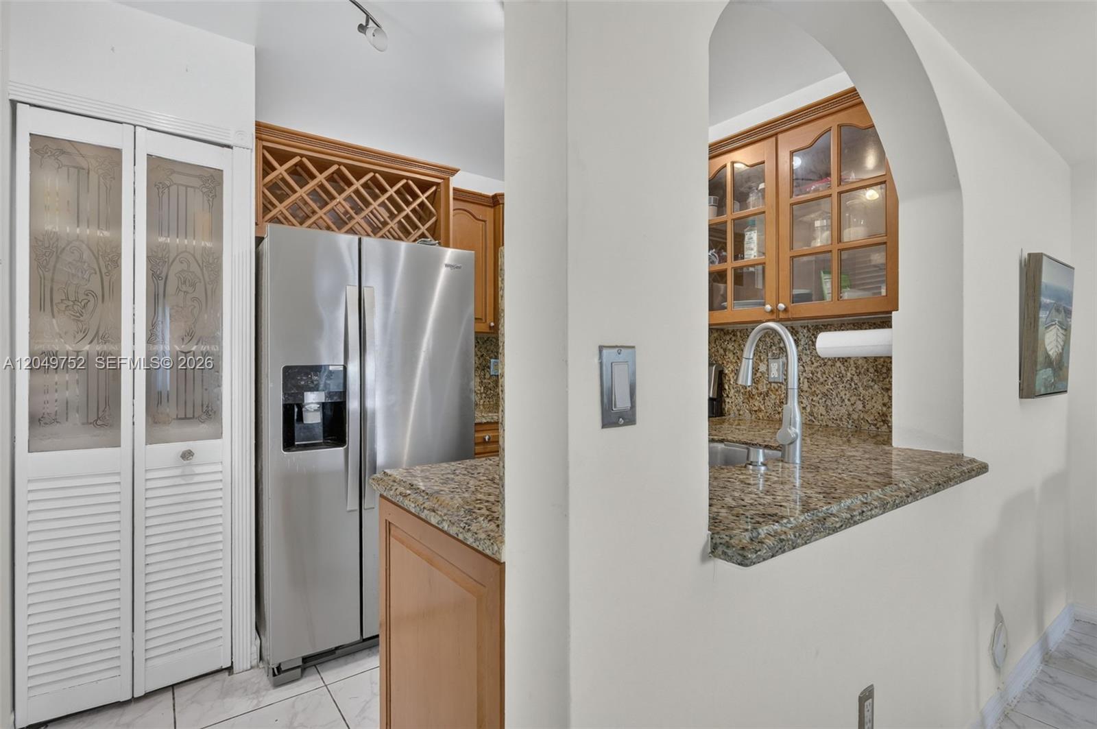 A kitchen features stainless steel appliances, granite countertops, and wood cabinetry viewed through an archway — 14929 SW 104th St # 14, Miami FL 33196, MIAMI, FL