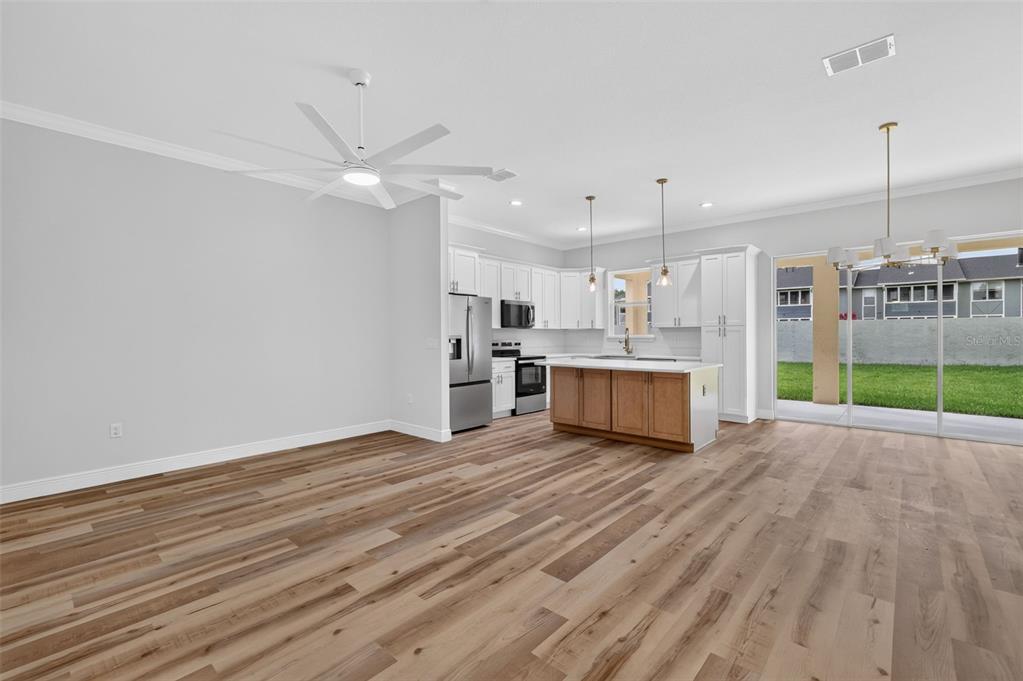 An open-concept kitchen and living area featuring wood-look flooring, white cabinetry, and a center island — 3045 SW 41ST PLACE, OCALA, FL