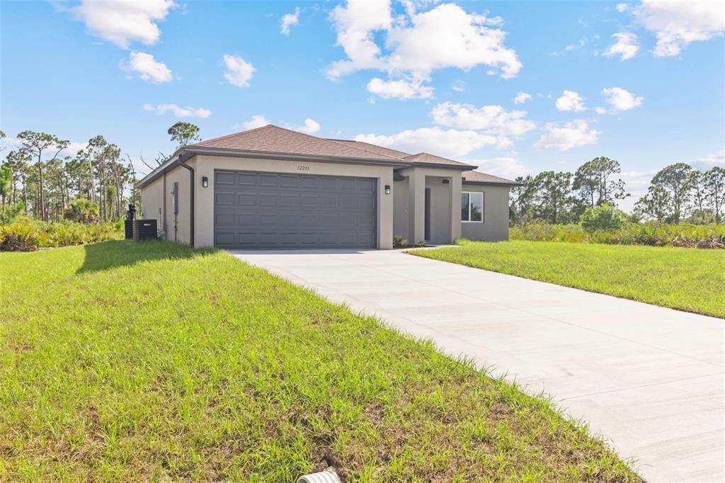 A single-story house with a gray garage, beige stucco exterior, and a concrete driveway — 12233 WAGNER LANE, PORT CHARLOTTE, FL