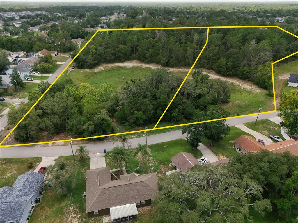 An aerial view shows two adjacent, partially wooded vacant lots outlined in yellow near residential homes — 2281 FAYSON LANE, SPRING HILL, FL