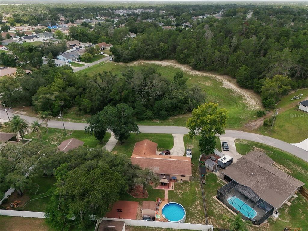 An aerial view shows a residential property with a pool, driveway, and surrounding wooded area — 2281 FAYSON LANE, SPRING HILL, FL
