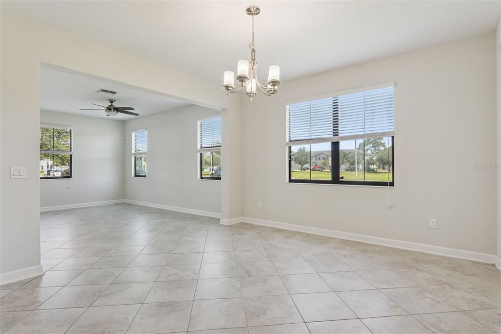 A bright dining area features a chandelier, tile flooring, and large windows with white blinds — 11433 WHISTLING PINE WAY, ORLANDO, FL