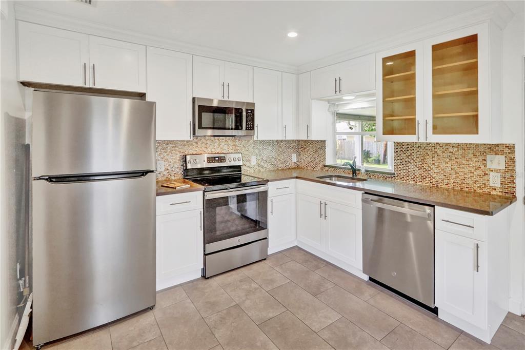 A kitchen with white cabinets, stainless steel appliances, brown countertops, and a mosaic tile backsplash — 1016 W SMITH STREET, ORLANDO, FL