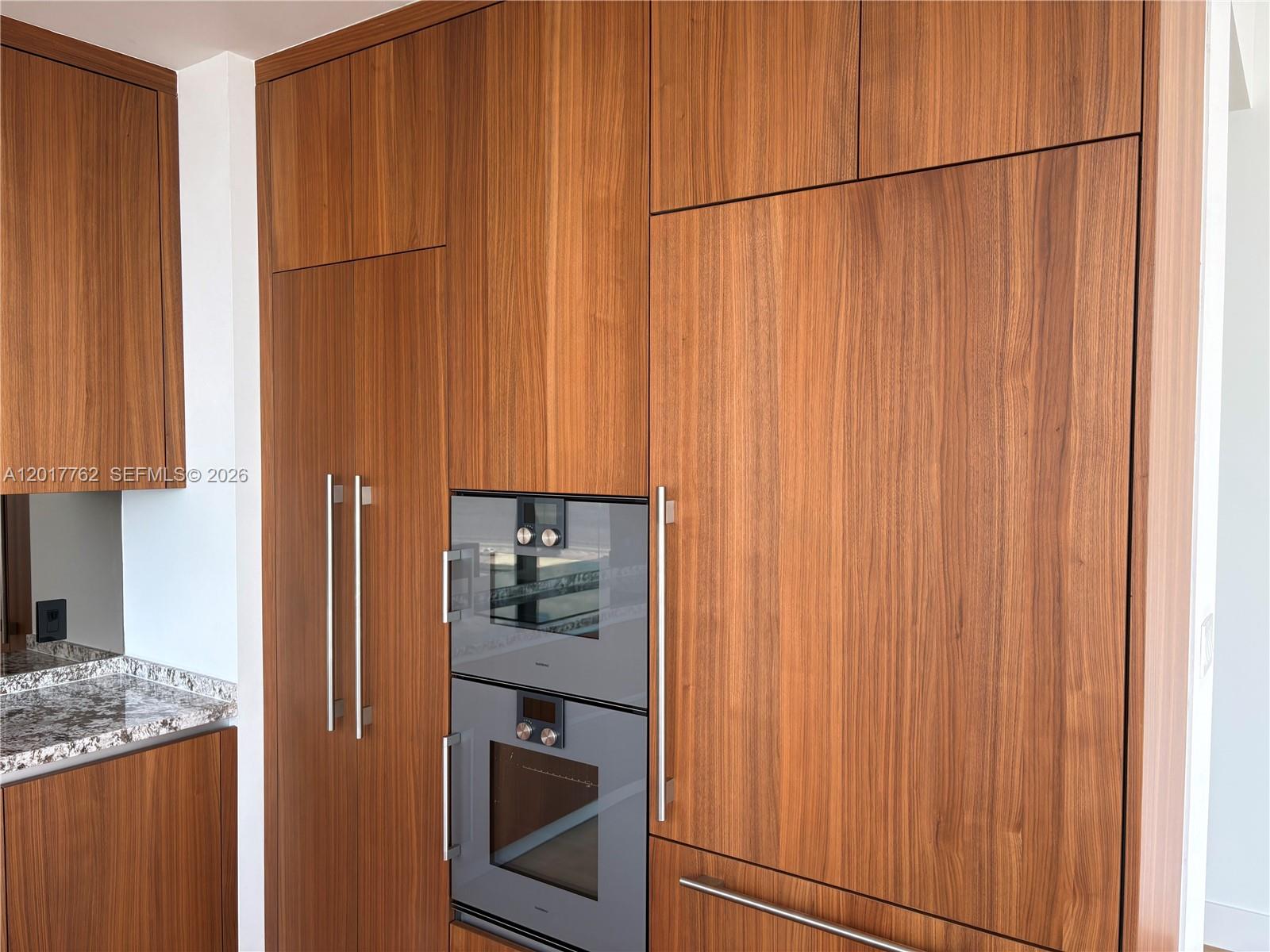 A kitchen wall features floor-to-ceiling wood cabinetry with integrated appliances and a granite countertop — 175 SE 25 Road # 602, Miami FL 33129, MIAMI, FL