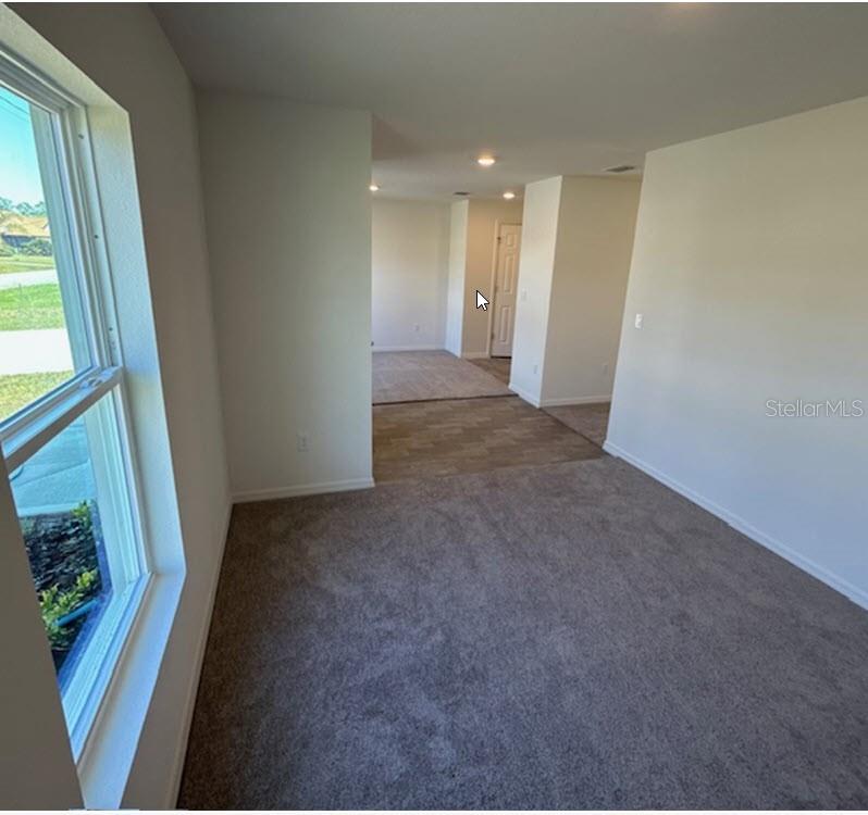 A room with gray carpeting transitions to a tiled hallway leading toward a closed door — 42 PEPPERCORN LANE, PALM COAST, FL