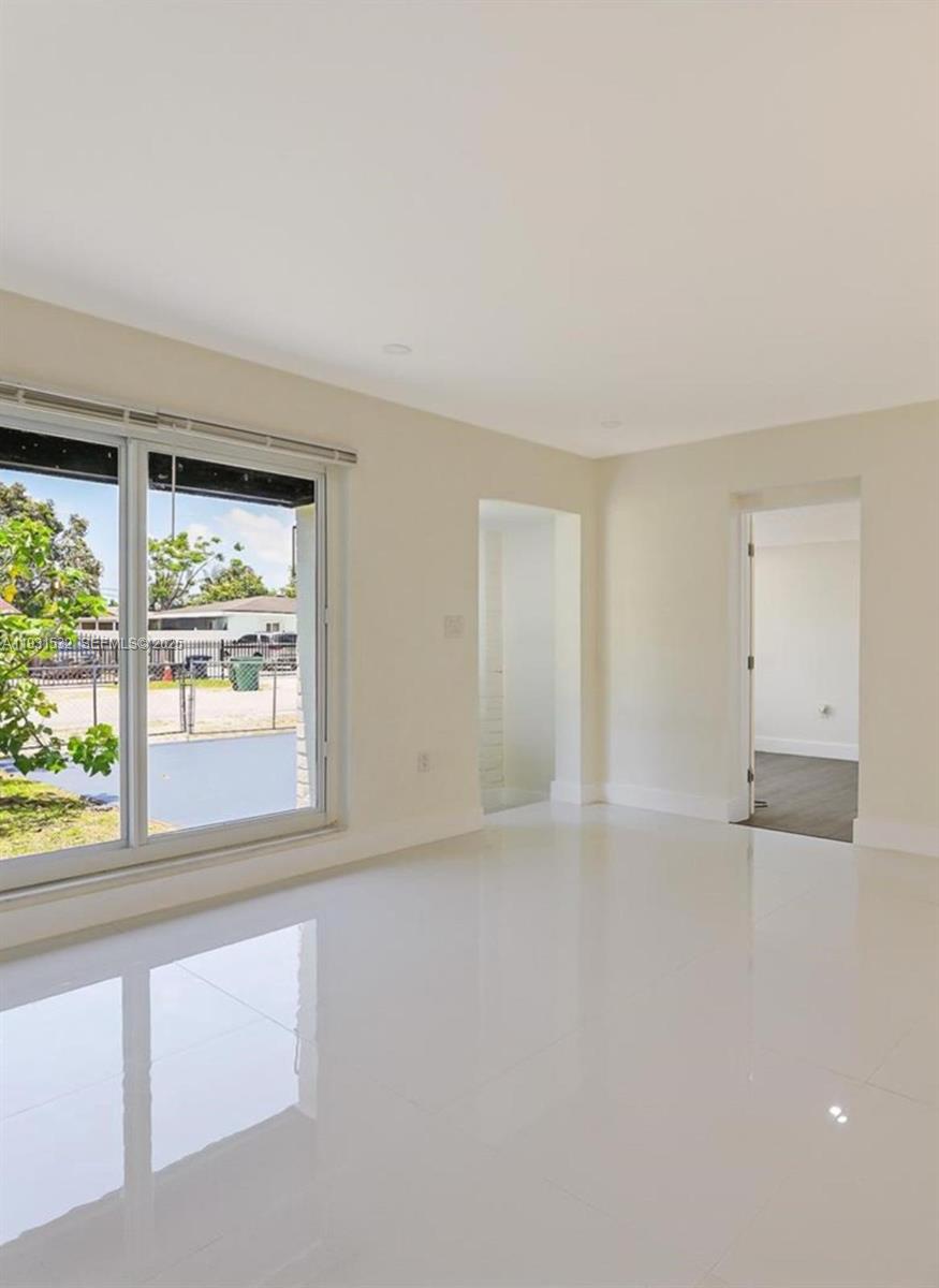 A bright, empty room features white tile floors, a large sliding glass door, and doorways — 851 NW 146th St, Miami FL 33168, MIAMI, FL