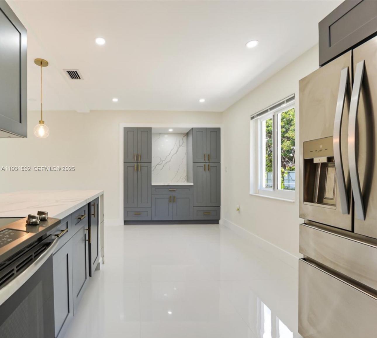 A modern kitchen features dark gray cabinetry, white marble countertops, and glossy white tile floors — 851 NW 146th St, Miami FL 33168, MIAMI, FL