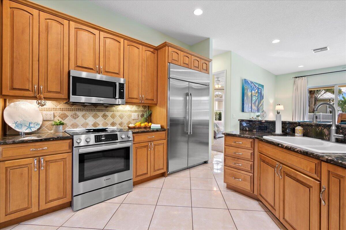 A kitchen with wood cabinets, stainless steel appliances, granite countertops, and light-colored tile flooring — 72 Waterway Road, Jupiter FL 33469, JUPITER, FL