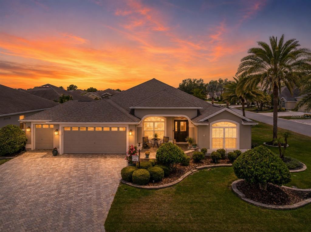 A single-story house with a paved driveway and a landscaped front yard at sunset — 1492 OLUSTEE PLACE, THE VILLAGES, FL