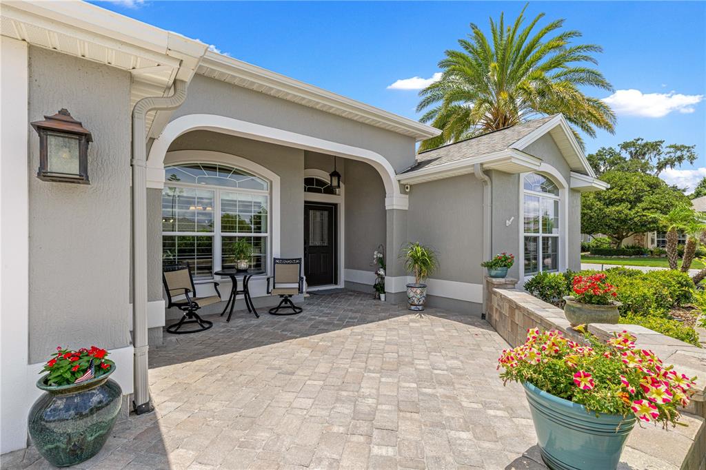A paved front patio features a seating area, potted flowers, and a covered entryway — 1492 OLUSTEE PLACE, THE VILLAGES, FL