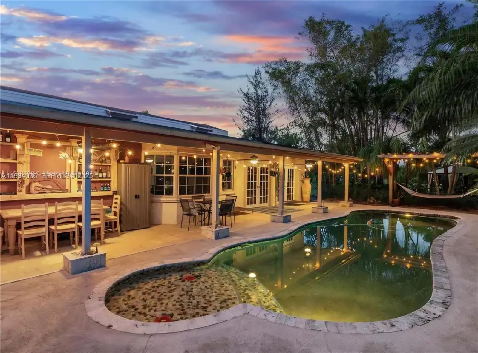 A backyard patio features a dining area, a swimming pool, and string lights at dusk — 19810 SW 200th St, Miami FL 33187, MIAMI, FL