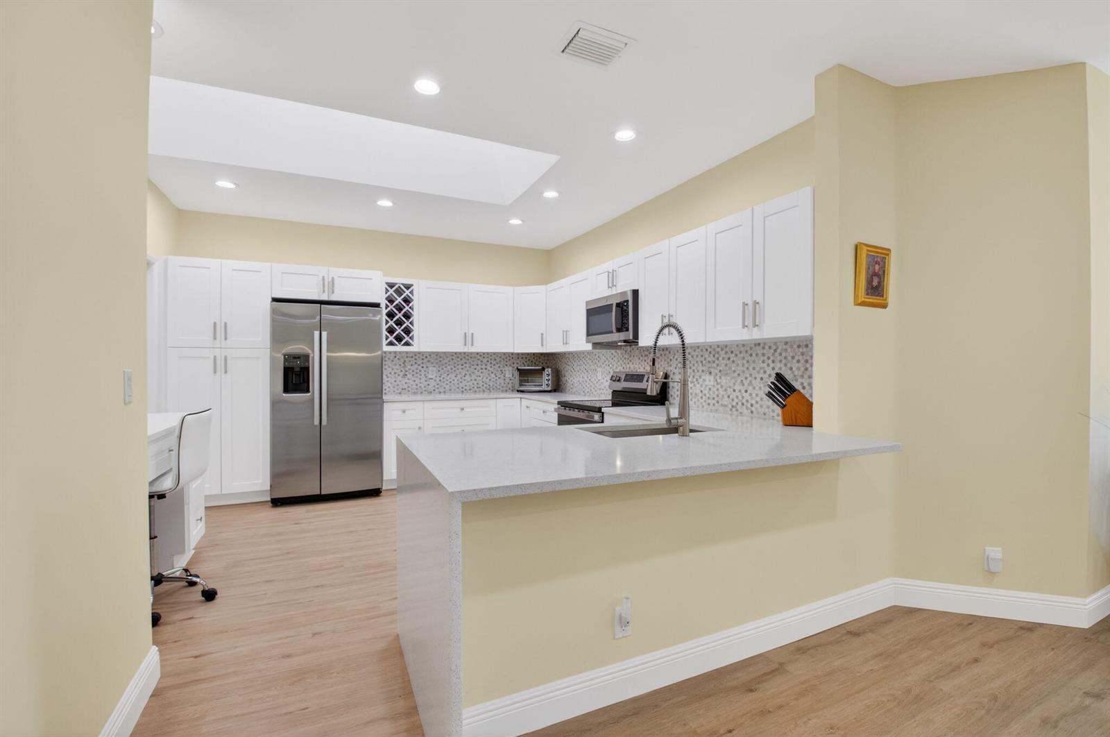 A kitchen features white cabinets, stainless steel appliances, a peninsula, and light-colored wood flooring — 8350 Springlake Drive, Boca Raton FL 33496, BOCA RATON, FL