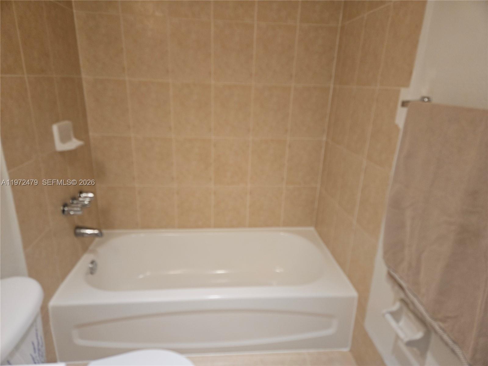 A bathroom features a white bathtub surrounded by tan tiled walls and a towel rack — 4550 NW 9th St # 704E, Miami FL 33126, MIAMI, FL