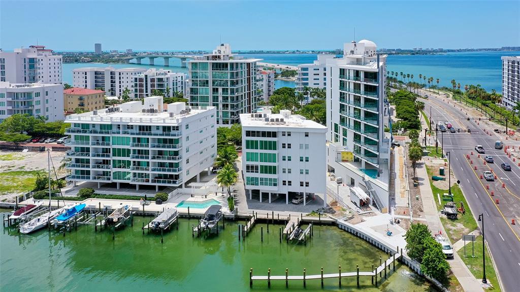 An aerial view shows waterfront apartment buildings with boat docks and a nearby coastal highway — 660 GOLDEN GATE POINT UNIT 51 & 52, SARASOTA, FL