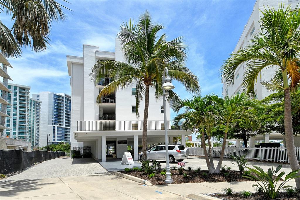 The exterior of a white multi-story apartment building features palm trees and a parking area — 660 GOLDEN GATE POINT UNIT 51 & 52, SARASOTA, FL